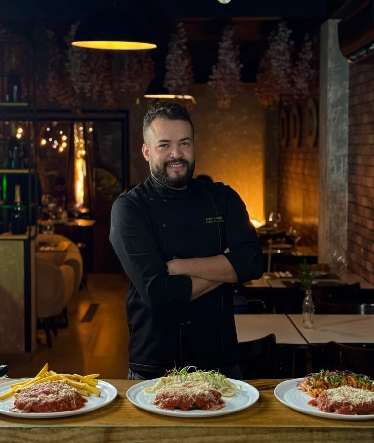 Chef Ivan Costa no salão de um restaurante, com pratos servidos à frente